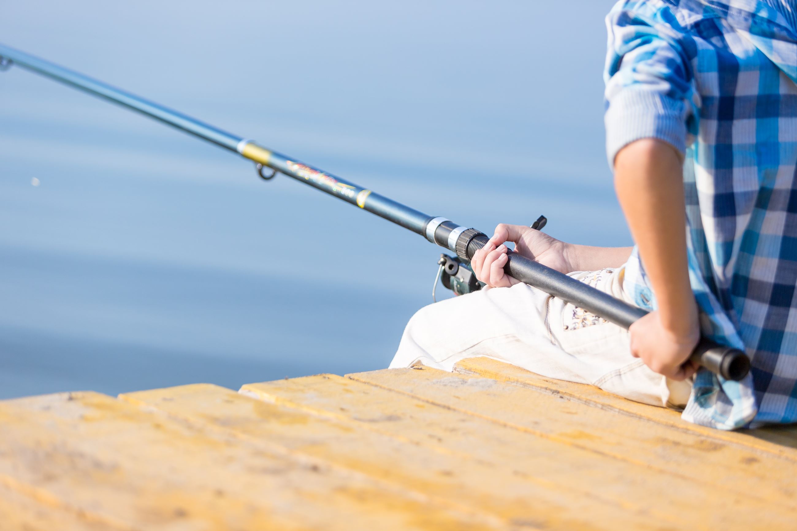 Person sitting on a wooden dock holding a fishing rod over calm water